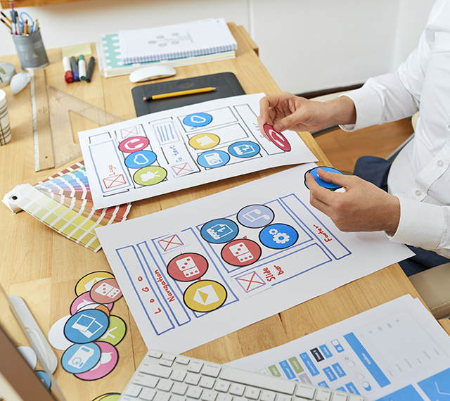 Creative web designer planning mobile application and developing template layout, spreading out paper icons